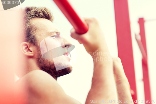 Image of young man exercising on horizontal bar outdoors