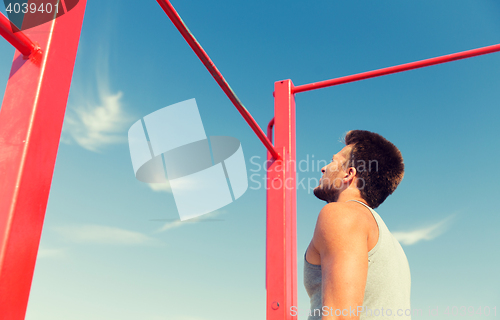 Image of young man exercising on horizontal bar outdoors