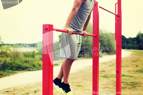 Image of young man exercising on horizontal bar outdoors