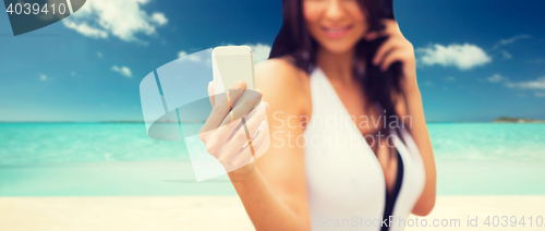 Image of young woman taking selfie with smartphone on beach