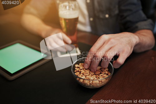 Image of man with tablet pc, beer and peanuts at bar or pub