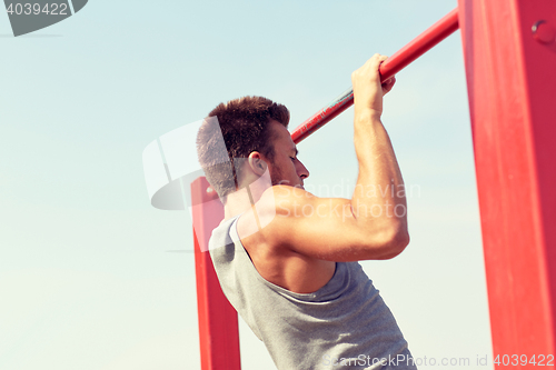 Image of young man exercising on horizontal bar outdoors