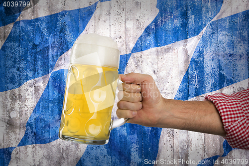 Image of Man in traditional Bavarian shirt holds mug of beer