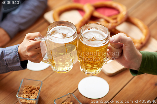 Image of close up of hands clinking beer mugs at bar or pub