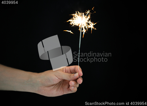Image of hand holding sparkler over black background