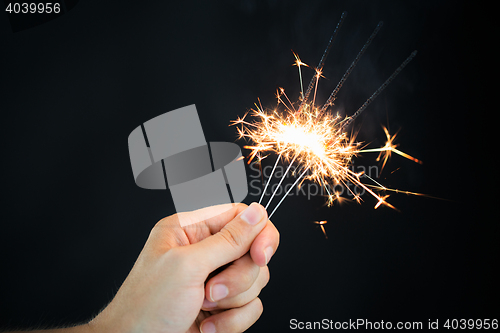 Image of hand holding sparklers over black background