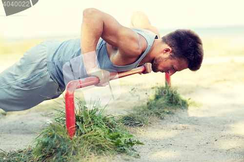 Image of young man exercising on horizontal bar outdoors