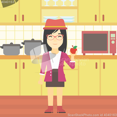 Image of Young woman with apple in the kitchen.