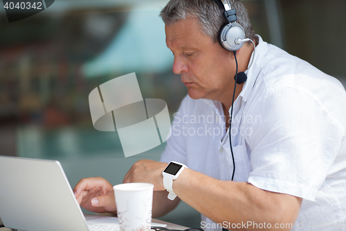 Image of Elderly man typing on laptop in cafe