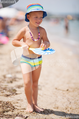 Image of Lovely smiling bot in hat walking on sandy beach