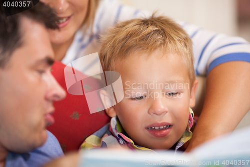 Image of Cute little boy reading a book with his parents