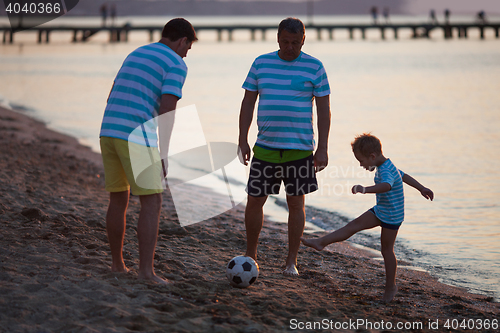 Image of Grandfather, Father and Son Kicking Ball on Beach