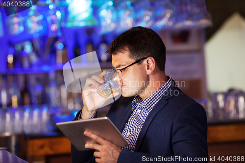 Image of Businessman with tablet drinking whisky in bar