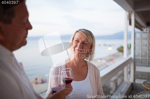 Image of Senior woman drinking wine with husband on balcony