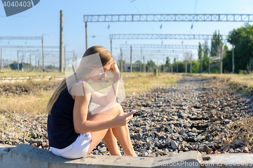 Image of Teenager girl with mobile sitting on unfinished rail track