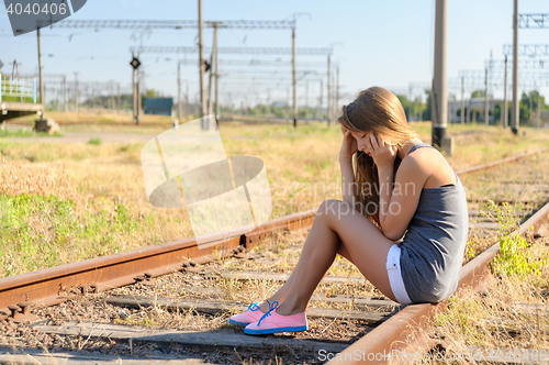 Image of Upset teenager girl sitting on rail track in countryside