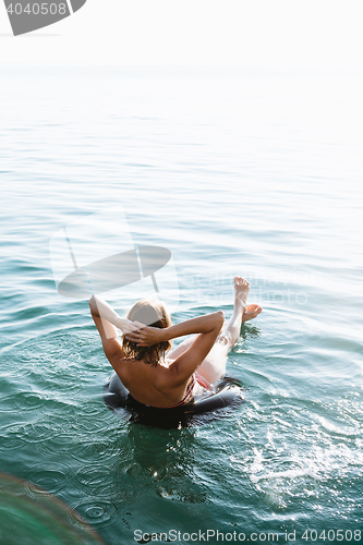 Image of Back view of relaxing woman floating on inflatable ring