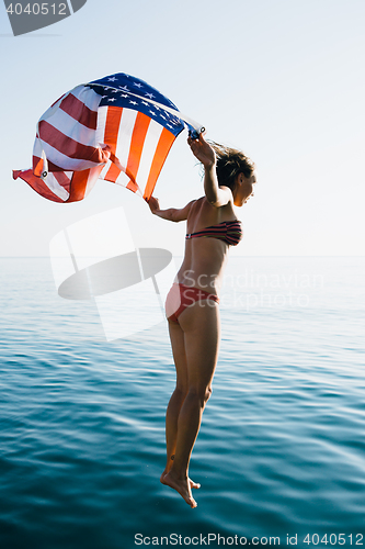 Image of Young woman in bikini jumping in water with American flag