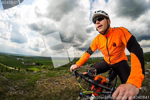 Image of Young man cycling on a rural road through green meadow