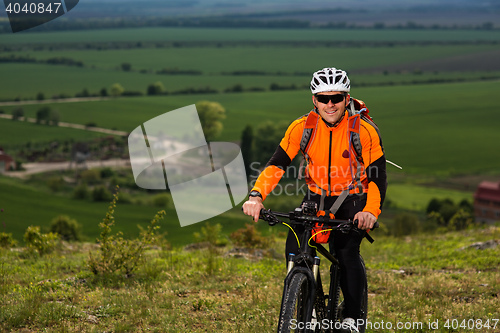 Image of Young man cycling on a rural road through green meadow