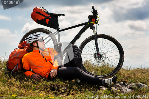 Image of Young man sitting near the cycle on a green meadow