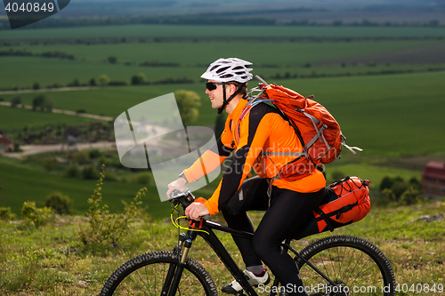 Image of Young man cycling on a rural road through green meadow