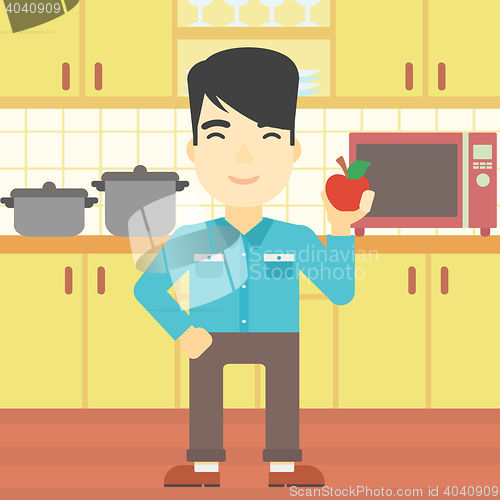 Image of Young man with apple in the kitchen.
