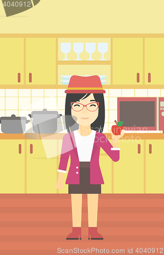 Image of Young woman with apple in the kitchen.