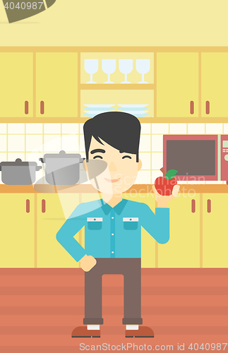 Image of Young man with apple in the kitchen.