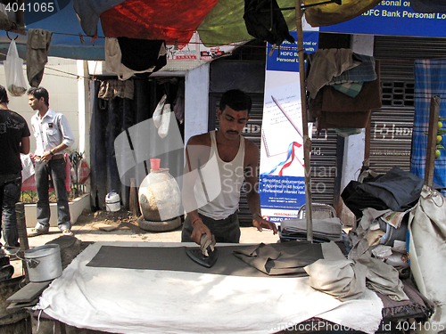Image of Streets of Kolkata. Man presses clothes using a traditional charcoal heated iron