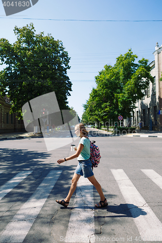 Image of young woman with backpack and coffee crossing the street