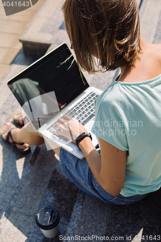 Image of Young short-haired girl working on laptop in sunlight