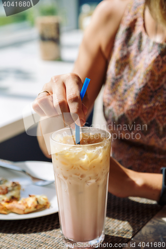 Image of Female hand stirring cold drink in glass with straw