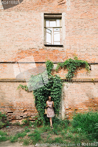 Image of Young woman in dress with coffee to go on green hedge