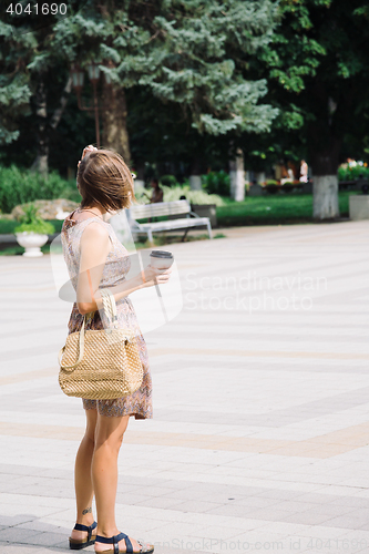 Image of Young brunette woman with coffee cup walking in city