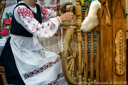 Image of Young woman spinning thread on a spinning wheel.