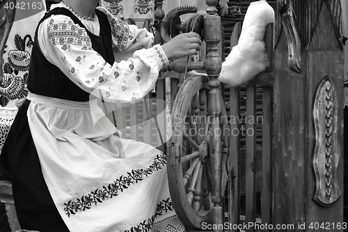 Image of Young woman spinning thread on a spinning wheel. Black-and-white