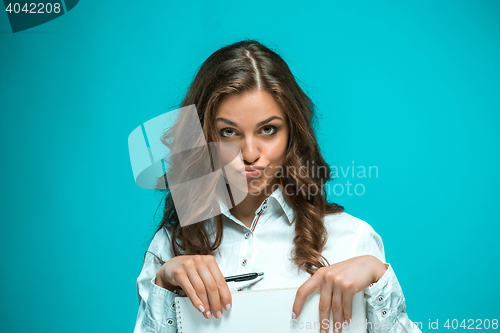 Image of The displeased young business woman with pen and tablet for notes on blue background