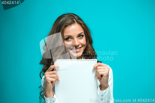 Image of The smiling young business woman with pen and tablet for notes on blue background