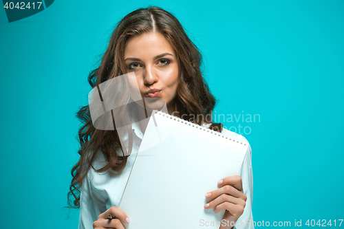 Image of The displeased young business woman with pen and tablet for notes on blue background