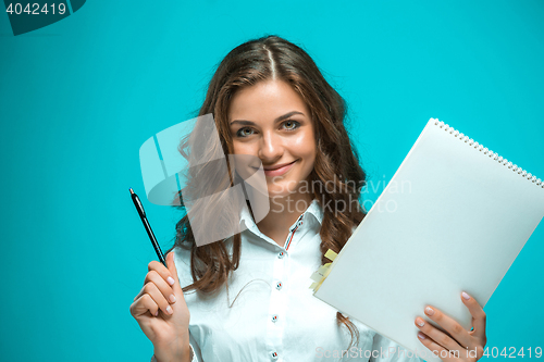 Image of The smiling young business woman with pen and tablet for notes on blue background