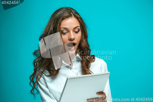 Image of Surprised young business woman with tablet for notes on blue background