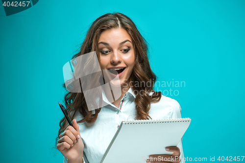 Image of Surprised young business woman with pen and tablet for notes on blue background