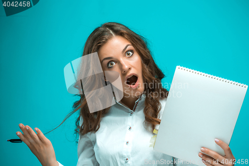 Image of Surprised young business woman with pen and tablet for notes on blue background