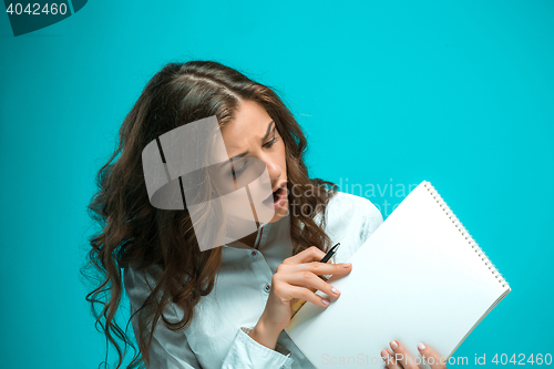 Image of Surprised young business woman with pen and tablet for notes on blue background