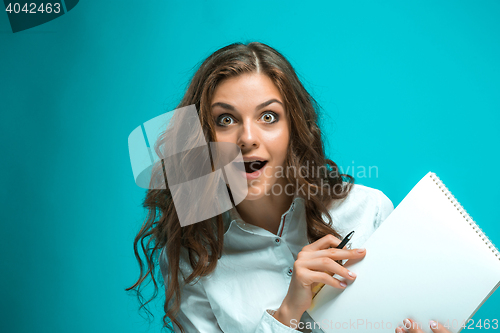 Image of Surprised young business woman with pen and tablet for notes on blue background
