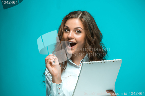 Image of Surprised young business woman with pen and tablet for notes on blue background
