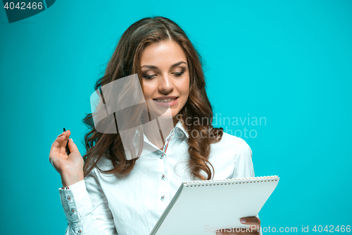 Image of Surprised young business woman with pen and tablet for notes on blue background