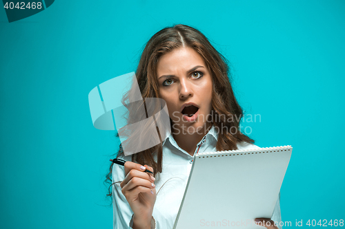 Image of Surprised young business woman with pen and tablet for notes on blue background