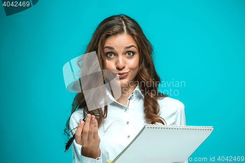 Image of Surprised young business woman with pen and tablet for notes on blue background